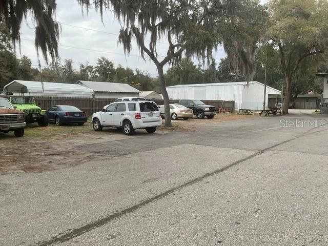 A gravel parking lot features several parked vehicles in front of two large metal buildings — 32416 COUNTY ROAD 473, LEESBURG, FL