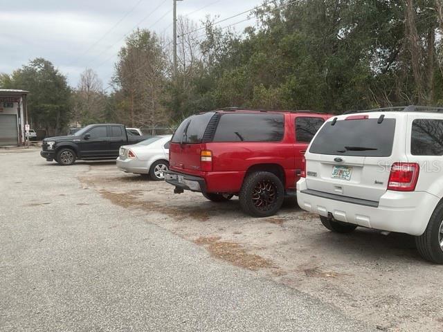 A gravel parking lot contains a black pickup truck, a silver sedan, and two SUVs — 32416 COUNTY ROAD 473, LEESBURG, FL