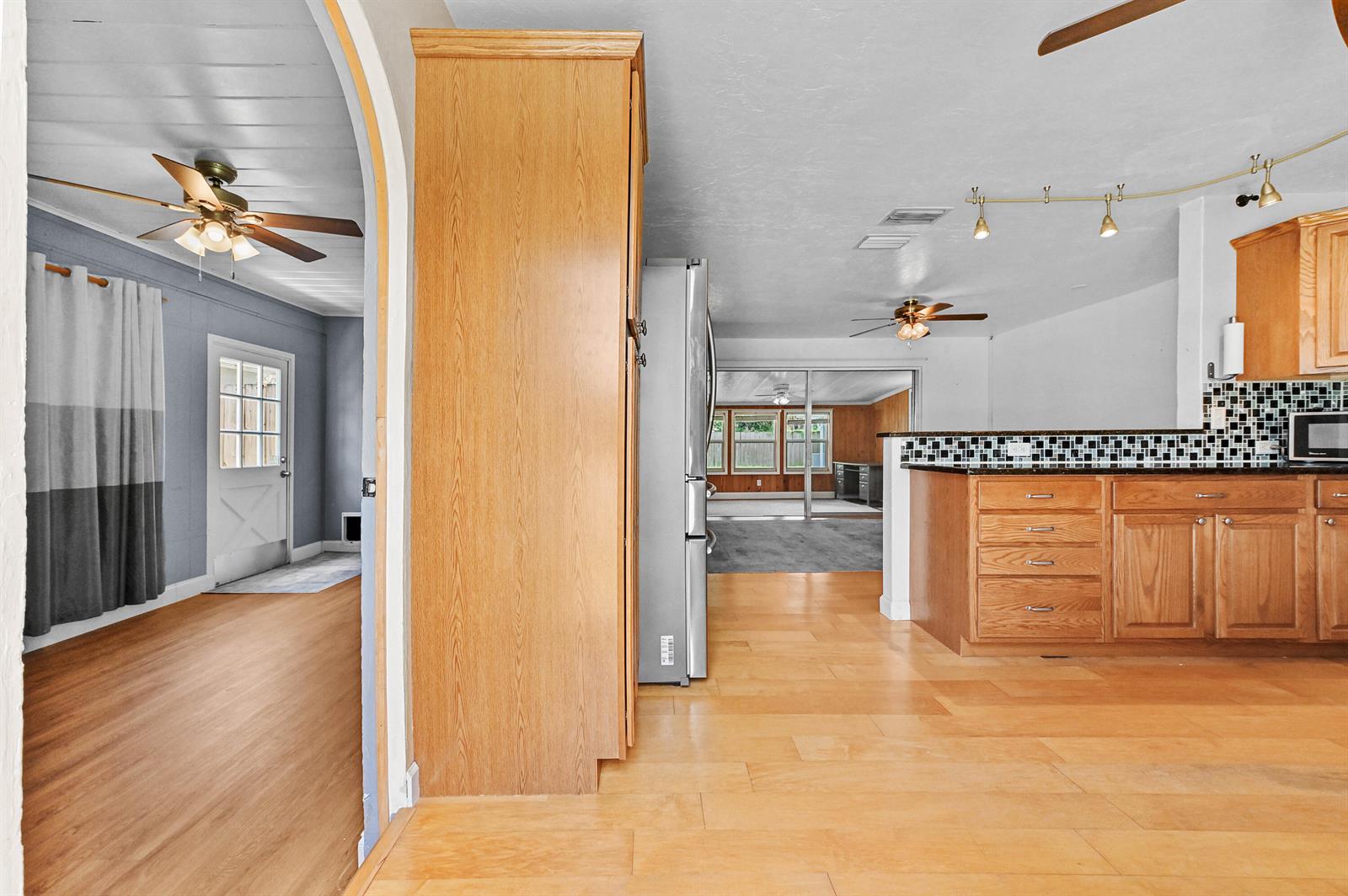 A kitchen with wood cabinets and a tile backsplash opens into a living area — 5709 SE Indigo Avenue, Stuart FL 34997, STUART, FL
