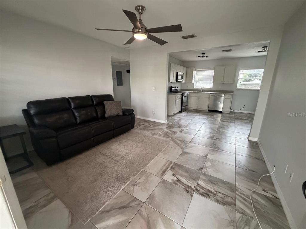 A living room with a dark leather sofa and tile floors opens into a kitchen — 4314 W CARMEN STREET, TAMPA, FL