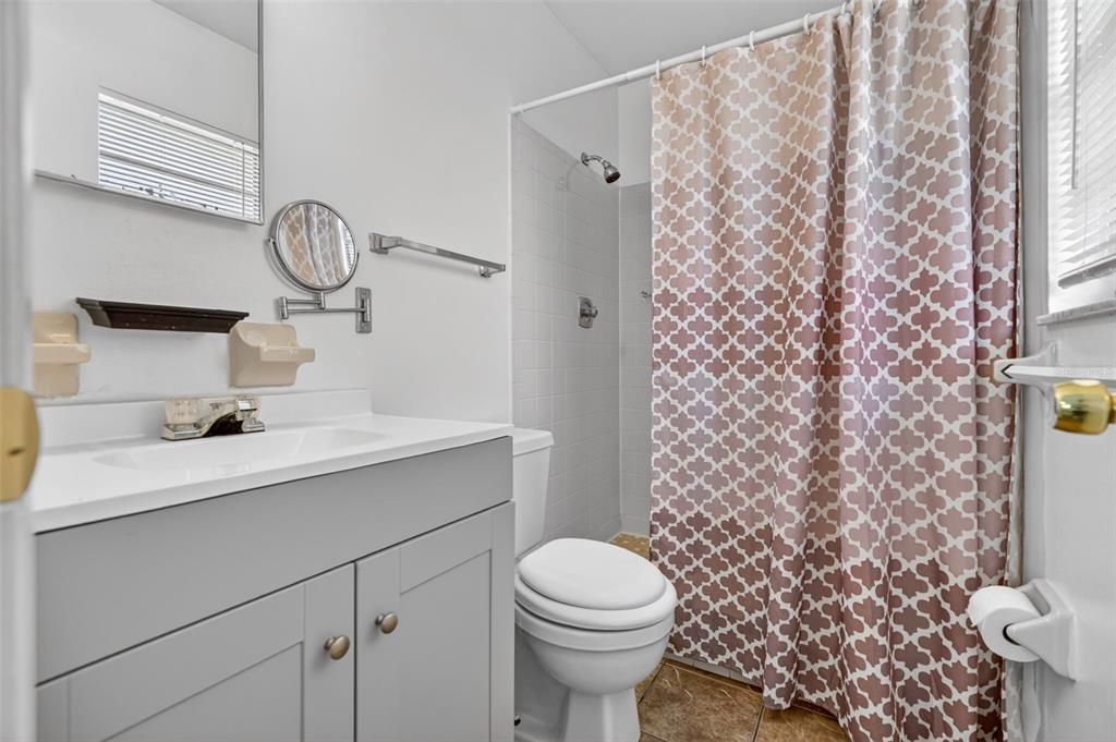 A bathroom features a gray vanity, a white toilet, and a shower with a patterned curtain — 2319 S TENNYSON POINT, HOMOSASSA, FL