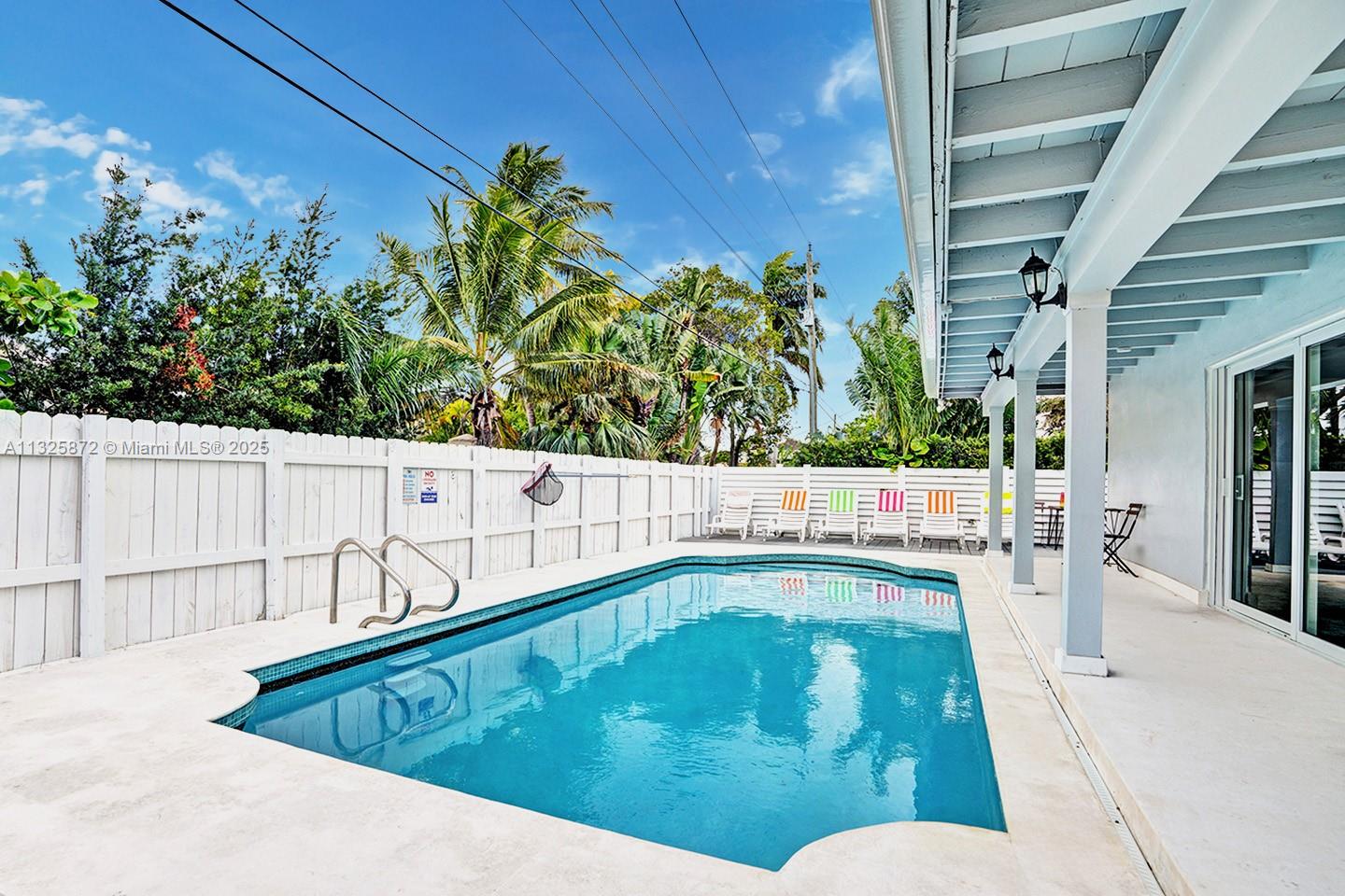 A backyard swimming pool sits next to a covered patio with a white fence — 1018 Adams St, Hollywood FL 33019, HOLLYWOOD, FL