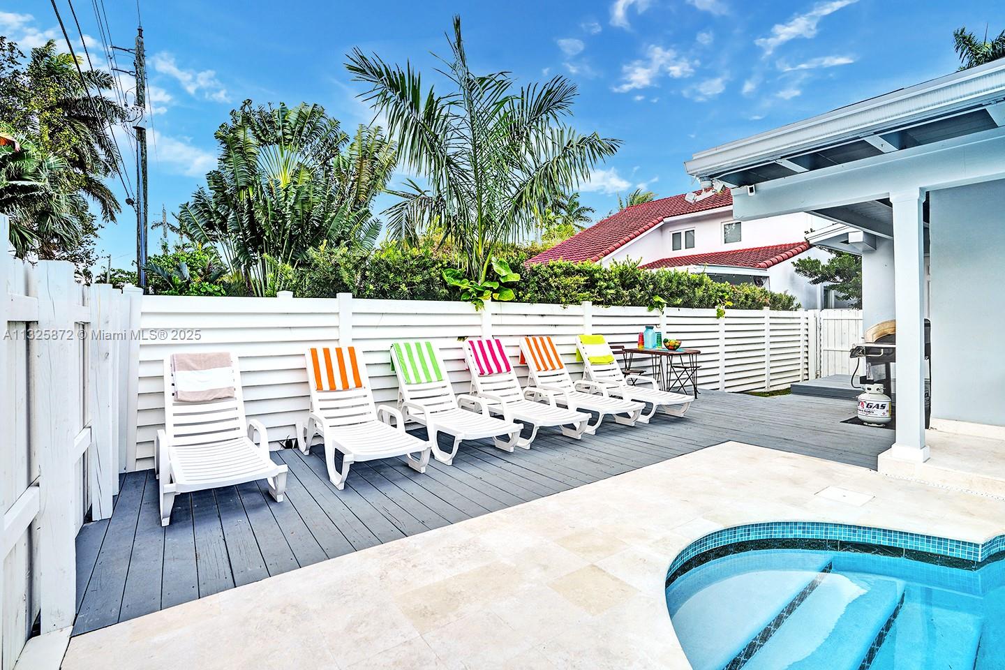 A backyard pool deck features several lounge chairs lined up against a white privacy fence — 1018 Adams St, Hollywood FL 33019, HOLLYWOOD, FL
