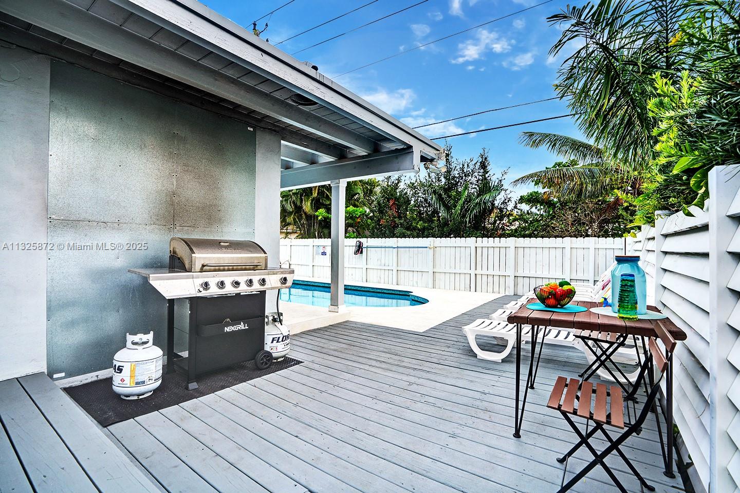 A wooden deck features a grill, dining set, and swimming pool enclosed by a white fence — 1018 Adams St, Hollywood FL 33019, HOLLYWOOD, FL