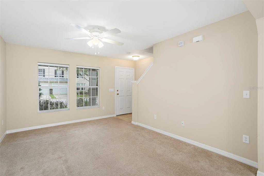 An empty living room features beige carpet, tan walls, a ceiling fan, and two windows — 2907 BEAR OAK DRIVE, VALRICO, FL