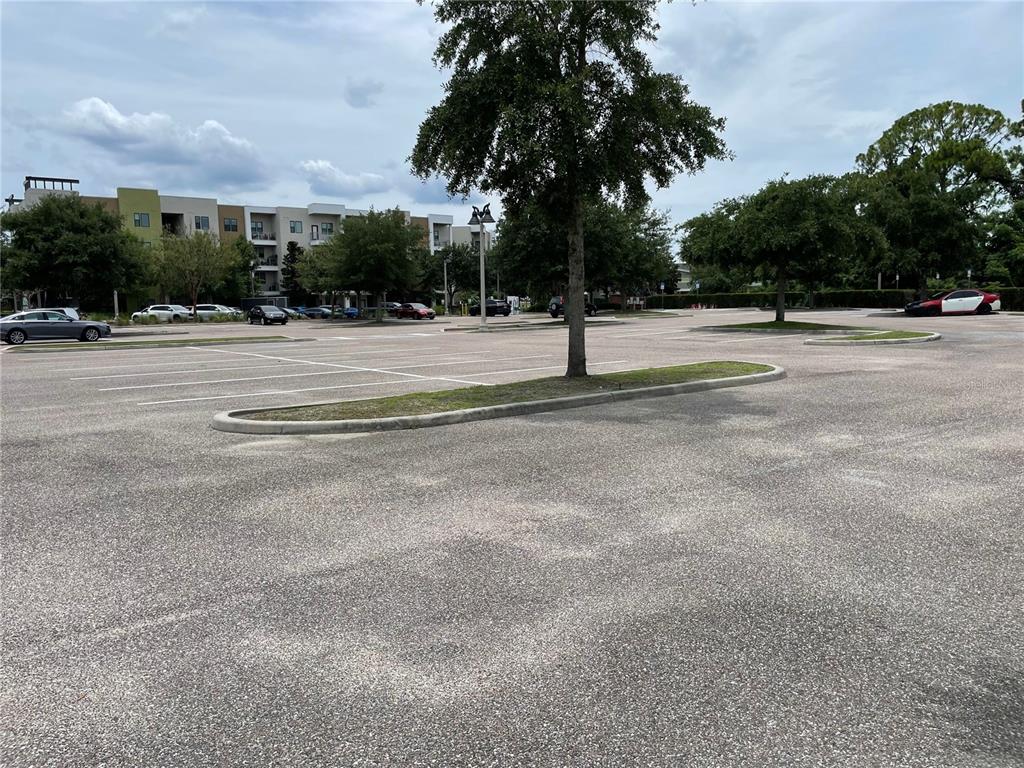 A large, paved parking lot features a central tree island and surrounding apartment buildings — Parcel 2 - 607 OVIEDO BLVD, OVIEDO, FL