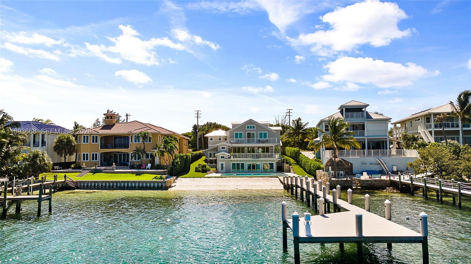 Three waterfront houses with private docks sit along a sandy beach under a blue sky — 18119 SE Federal Hwy, Jupiter FL 33469, JUPITER, FL