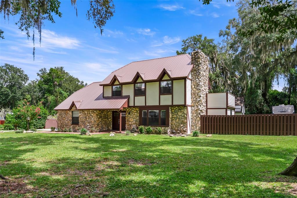 A two-story house with a stone facade, brown metal roof, and a large stone chimney — 102 THICKET LANE, PALATKA, FL