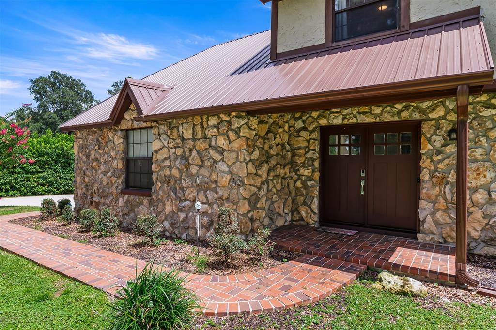 A stone-faced house exterior features a brown metal roof and a brick walkway — 102 THICKET LANE, PALATKA, FL