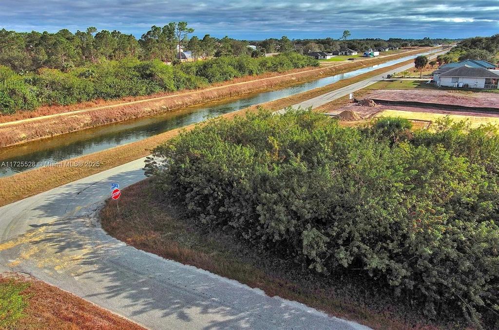 An aerial view shows a paved road, a canal, and a vacant lot with vegetation — 4506 E 19TH STREET, LEHIGH ACRES, FL