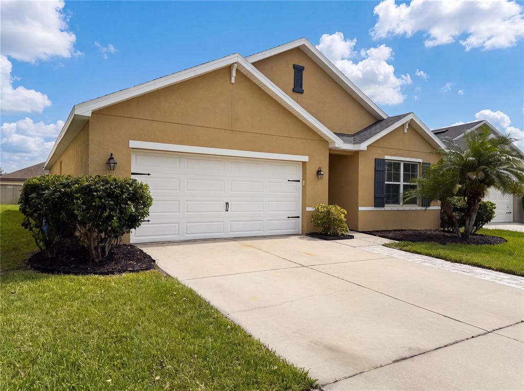 A tan, single-story suburban house with a white two-car garage and a paved driveway — 16415 TREASURE POINT DRIVE, WIMAUMA, FL