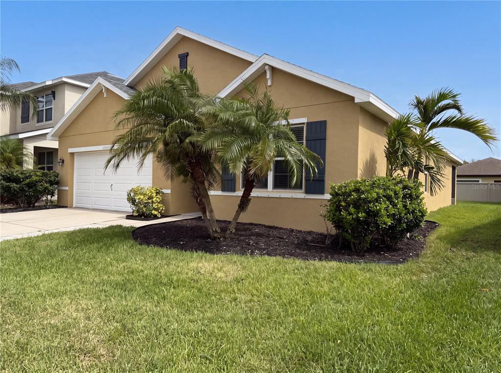 A single-story tan house with a two-car garage, palm trees, and dark shutters — 16415 TREASURE POINT DRIVE, WIMAUMA, FL