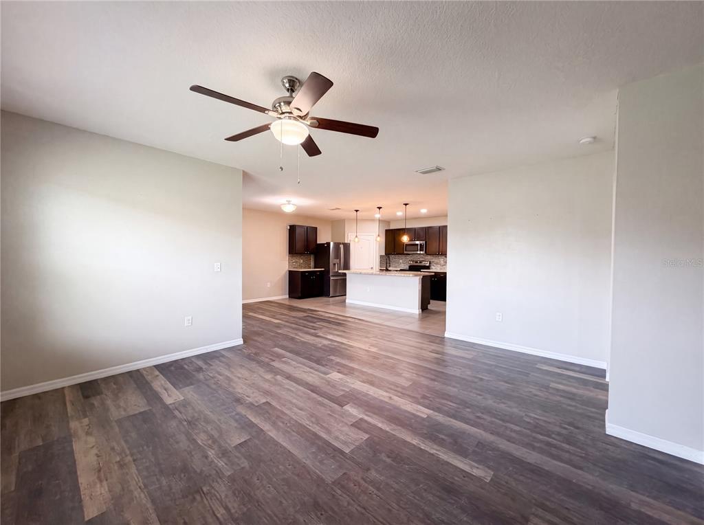 An open-concept living area features wood-look flooring, a ceiling fan, and a kitchen with island — 16415 TREASURE POINT DRIVE, WIMAUMA, FL