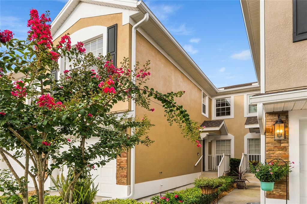 A two-story townhouse exterior with tan stucco walls, stone accents, and a flowering crape myrtle — 417 HILGARD COVE UNIT ., SANFORD, FL