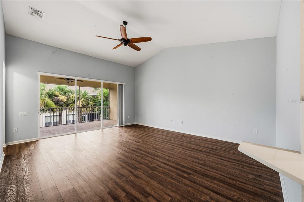 An empty living room features dark wood-look flooring, a vaulted ceiling, and a sliding glass door — 417 HILGARD COVE UNIT ., SANFORD, FL
