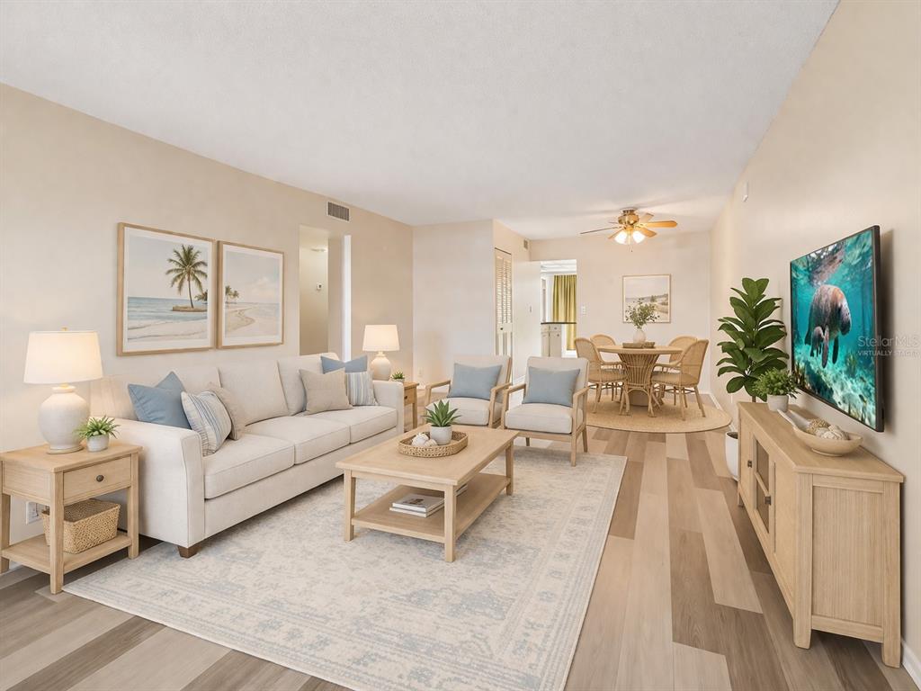 A living room with light wood flooring, a beige sofa, and a wall-mounted television — 5095 BAY STREET NE UNIT 110, ST PETERSBURG, FL