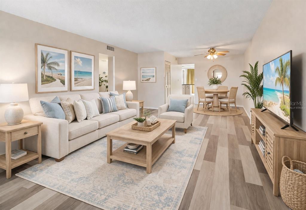 A living room with light wood flooring, a beige sofa, and a dining area beyond — 5095 BAY STREET NE UNIT 110, ST PETERSBURG, FL