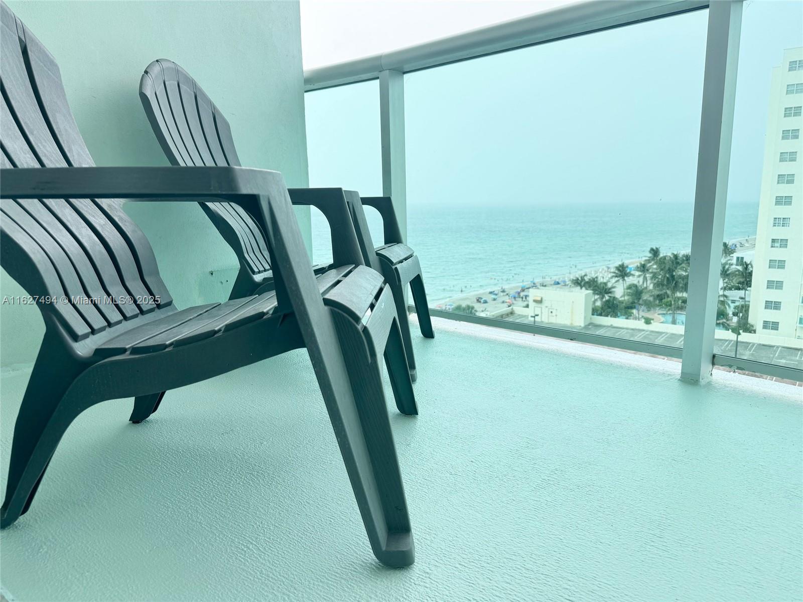 Two dark plastic chairs sit on a light blue balcony overlooking the ocean and beach — 3801 OCEAN DR # 10H, Hollywood FL 33019, HOLLYWOOD, FL