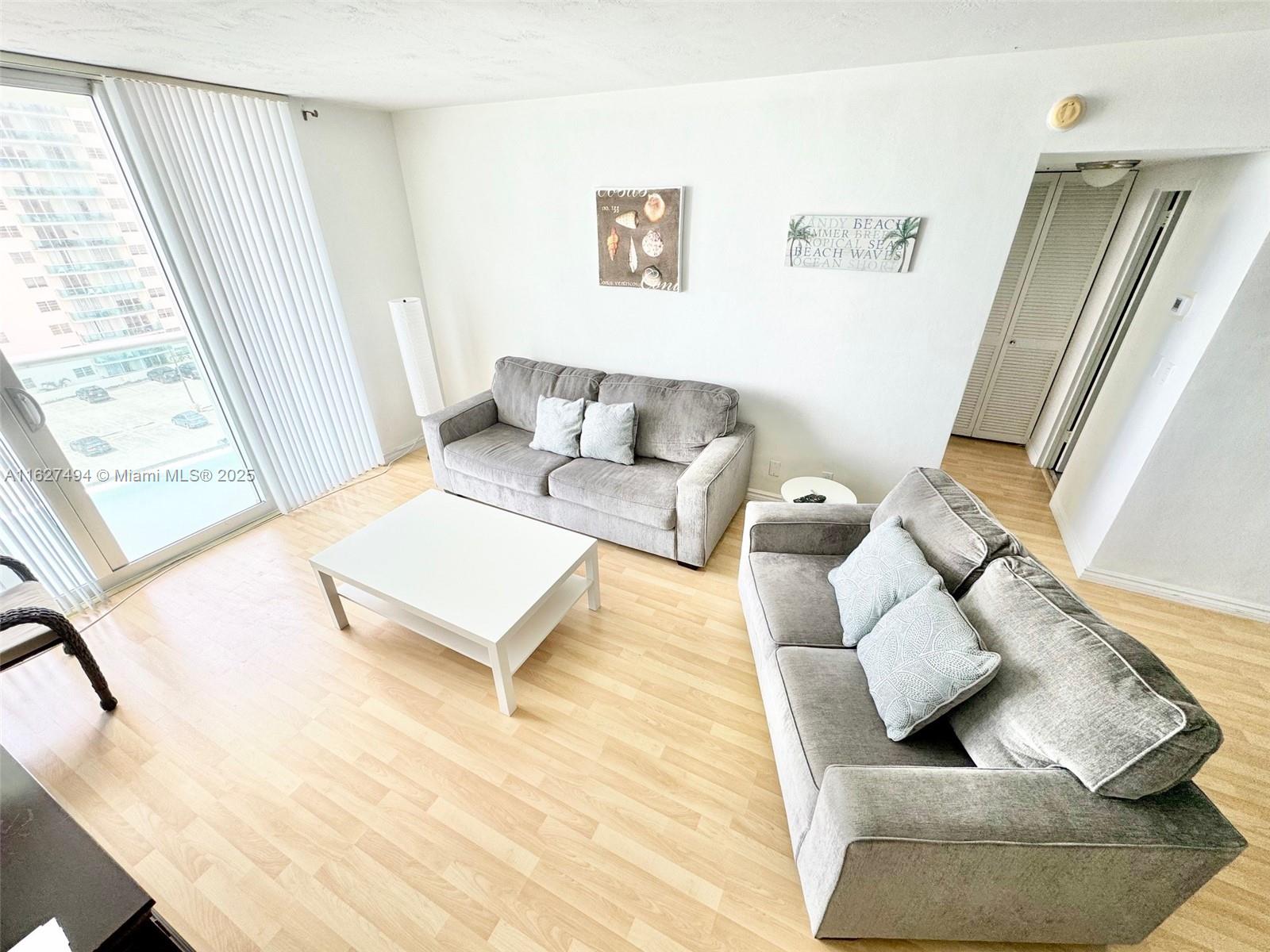 A living room features two gray sofas, a white coffee table, and light wood flooring — 3801 OCEAN DR # 10H, Hollywood FL 33019, HOLLYWOOD, FL