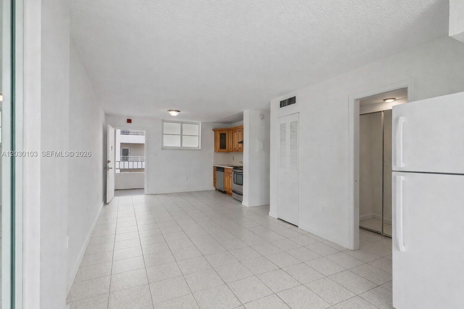 An open-concept kitchen and living area features white tile flooring and a balcony entrance — 1750 James Ave # 9C, Miami Beach FL 33139, MIAMI BEACH, FL