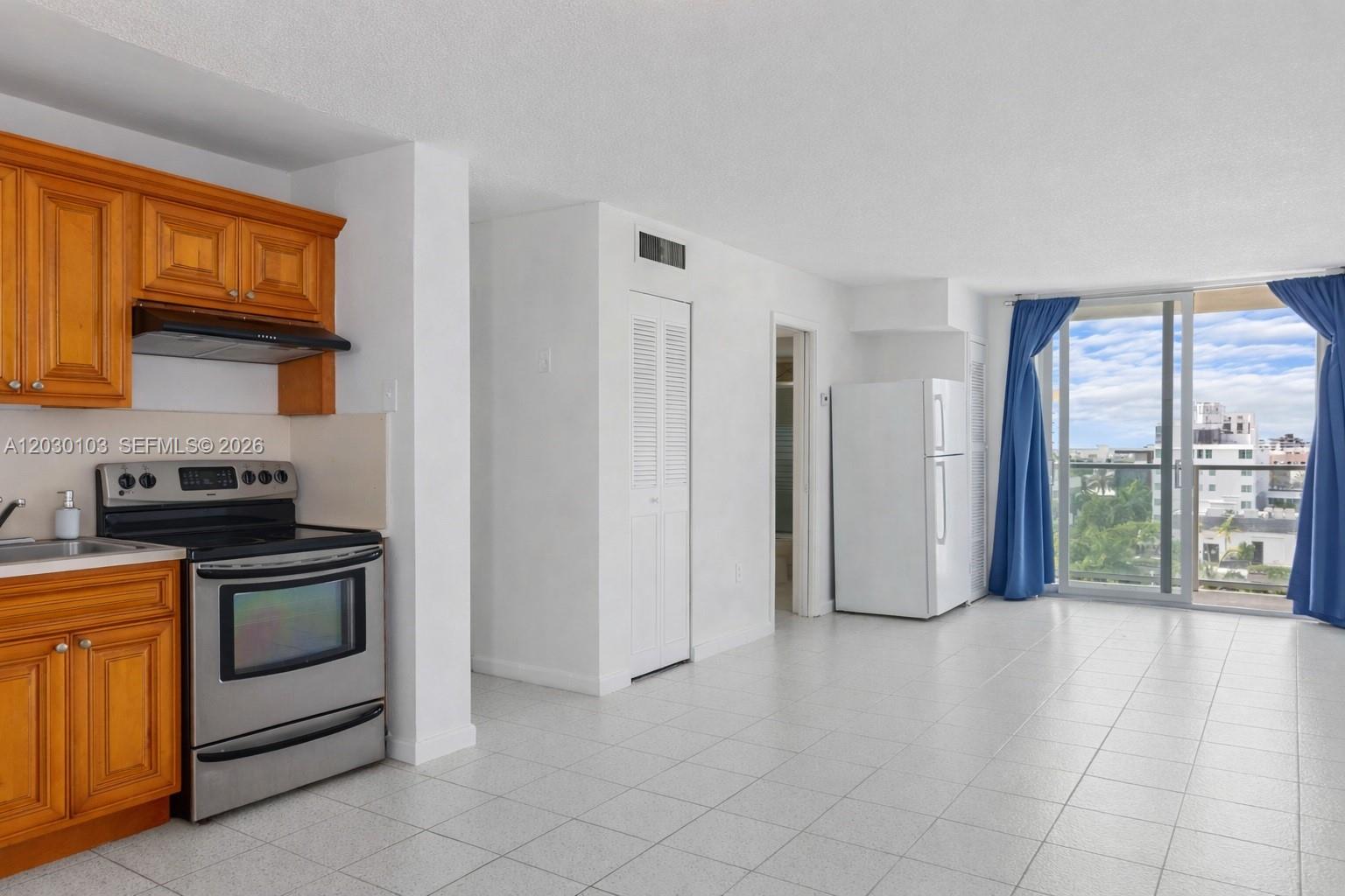 A kitchen with wood cabinets and stainless steel appliances opens to a bright living area — 1750 James Ave # 9C, Miami Beach FL 33139, MIAMI BEACH, FL