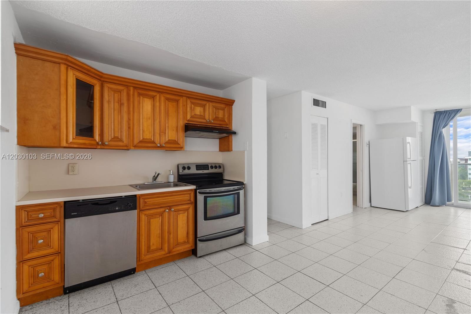 A kitchen features wooden cabinets, stainless steel appliances, and white tile flooring — 1750 James Ave # 9C, Miami Beach FL 33139, MIAMI BEACH, FL