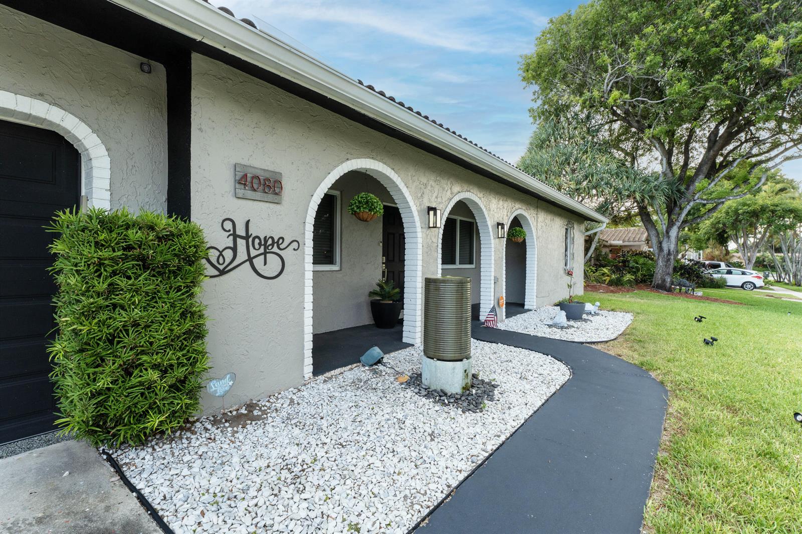 A stucco house exterior features arched entryways, a dark walkway, and white gravel landscaping — 4080 Lake Drive, Coconut Creek FL 33066, COCONUT CREEK, FL