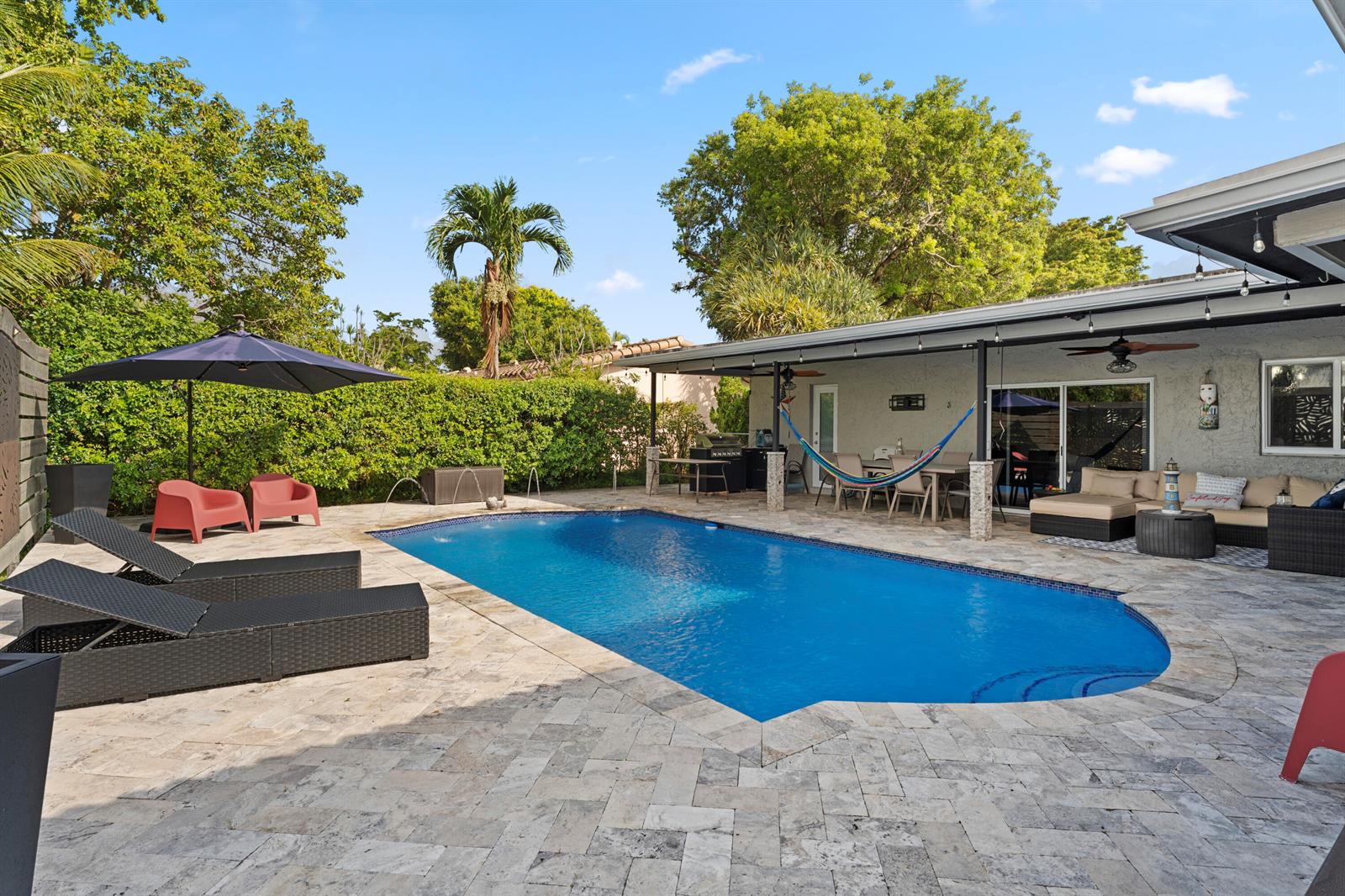 A backyard features a swimming pool, stone patio, lounge chairs, and a covered patio area — 4080 Lake Drive, Coconut Creek FL 33066, COCONUT CREEK, FL