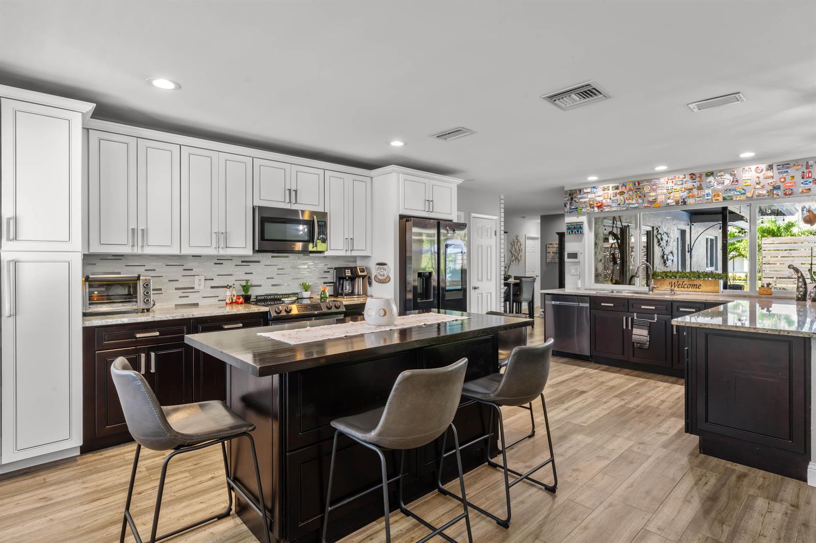 A kitchen features white upper cabinets, dark lower cabinets, a central island, and wood-look flooring — 4080 Lake Drive, Coconut Creek FL 33066, COCONUT CREEK, FL