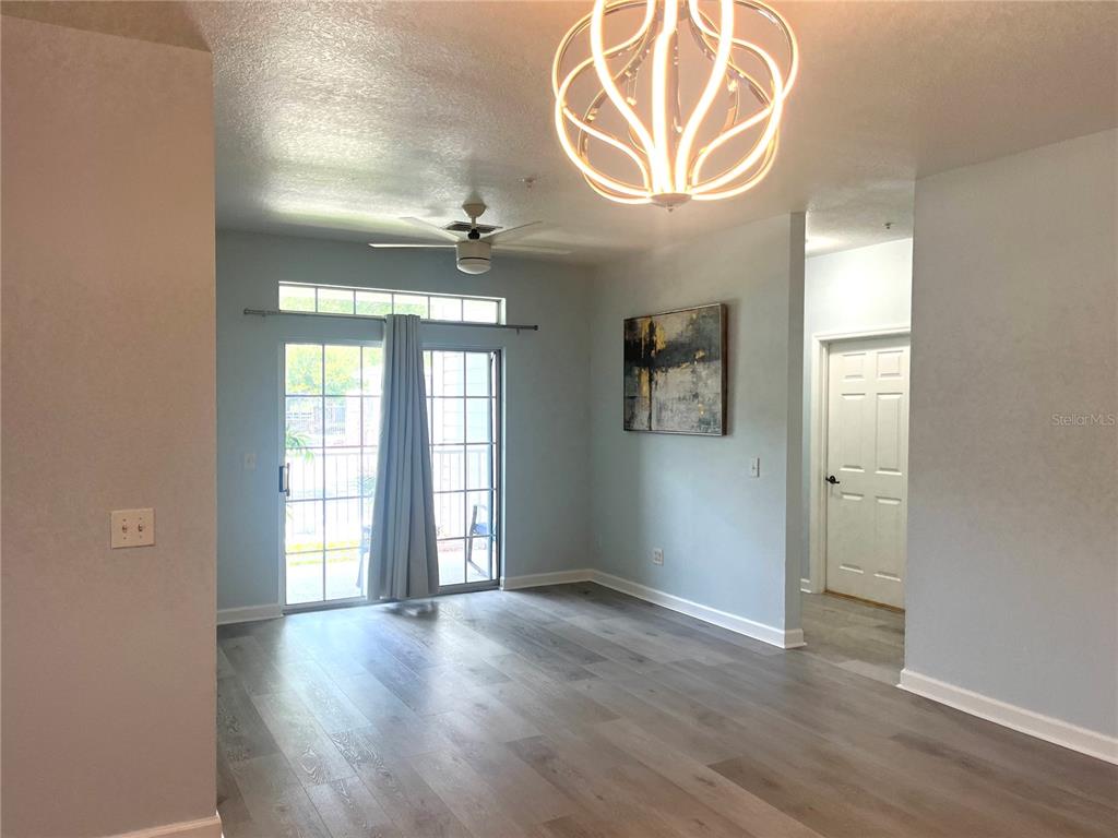 An interior room features light-colored wood-look flooring, a modern chandelier, and sliding glass balcony doors — 3177 FELTRIM PLACE UNIT 101, KISSIMMEE, FL