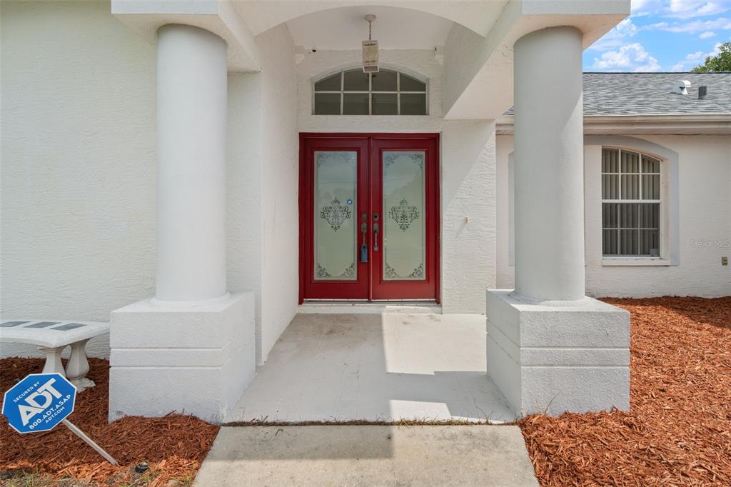 A front entrance features a red double door with glass inserts between two white columns — 7401 BLACKBIRD AVENUE, WEEKI WACHEE, FL