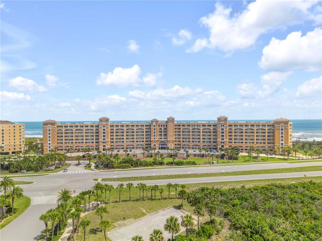 An aerial view of a large, multi-story oceanfront resort building with palm trees and landscaping — 60 SURFVIEW DRIVE UNIT 510, PALM COAST, FL
