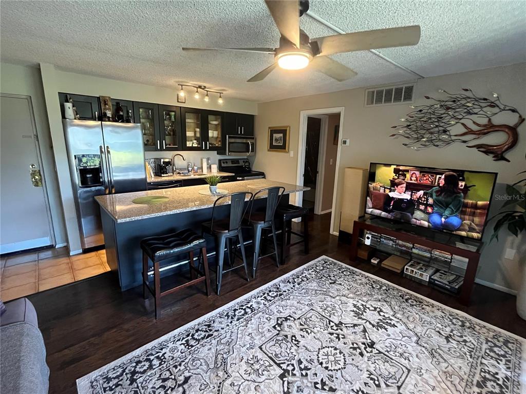 An open-concept kitchen with a granite island and dark cabinets overlooks a living area — 2632 HIDDEN LAKE DR N UNIT B, SARASOTA, FL