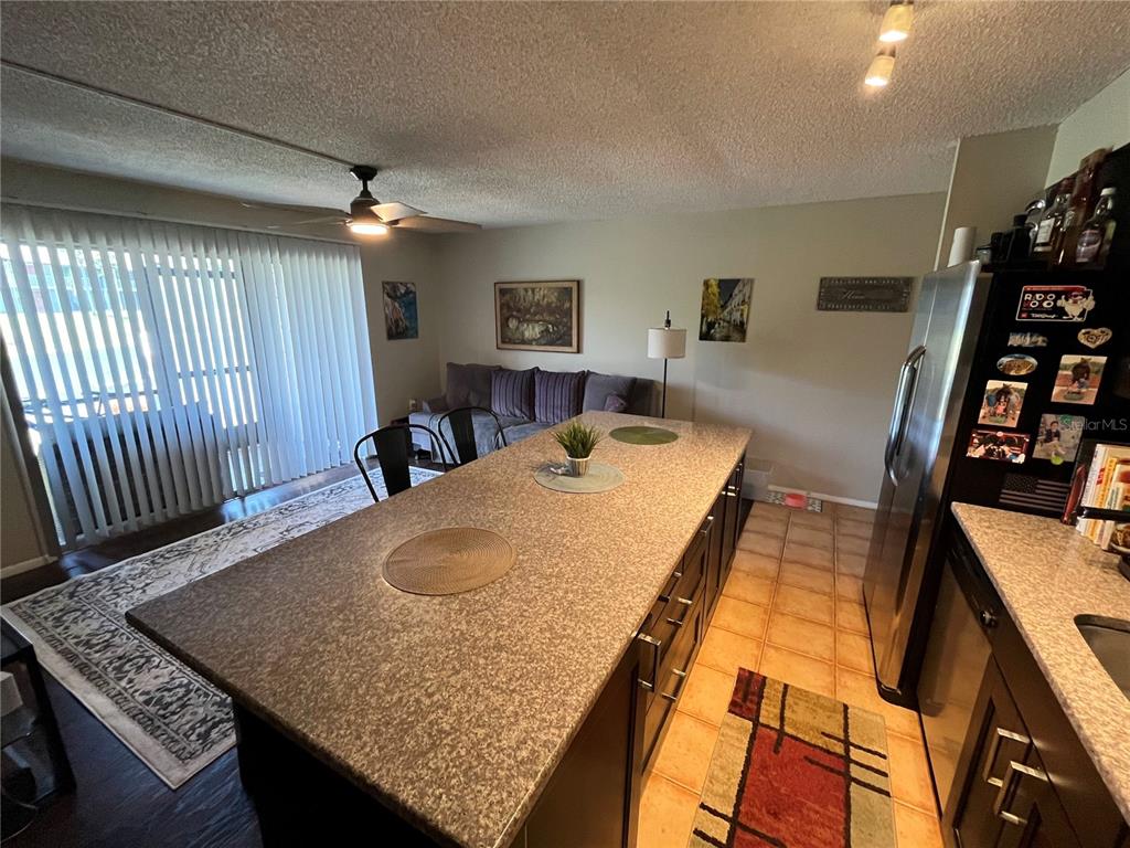 A kitchen island with a granite countertop sits in front of a living area — 2632 HIDDEN LAKE DR N UNIT B, SARASOTA, FL