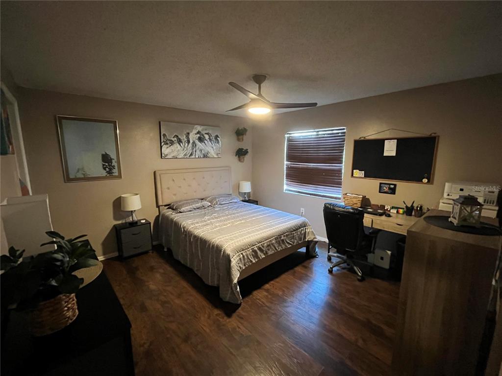 A bedroom features a bed, a desk with a chair, and dark wood flooring — 2632 HIDDEN LAKE DR N UNIT B, SARASOTA, FL