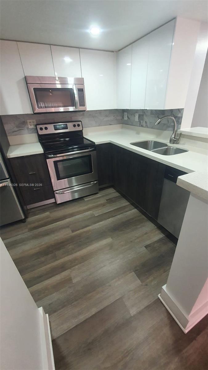 A kitchen features white upper cabinets, dark lower cabinets, stainless steel appliances, and wood-look flooring — 9885 Nob Hill Ct # 9885, Sunrise FL 33351, SUNRISE, FL