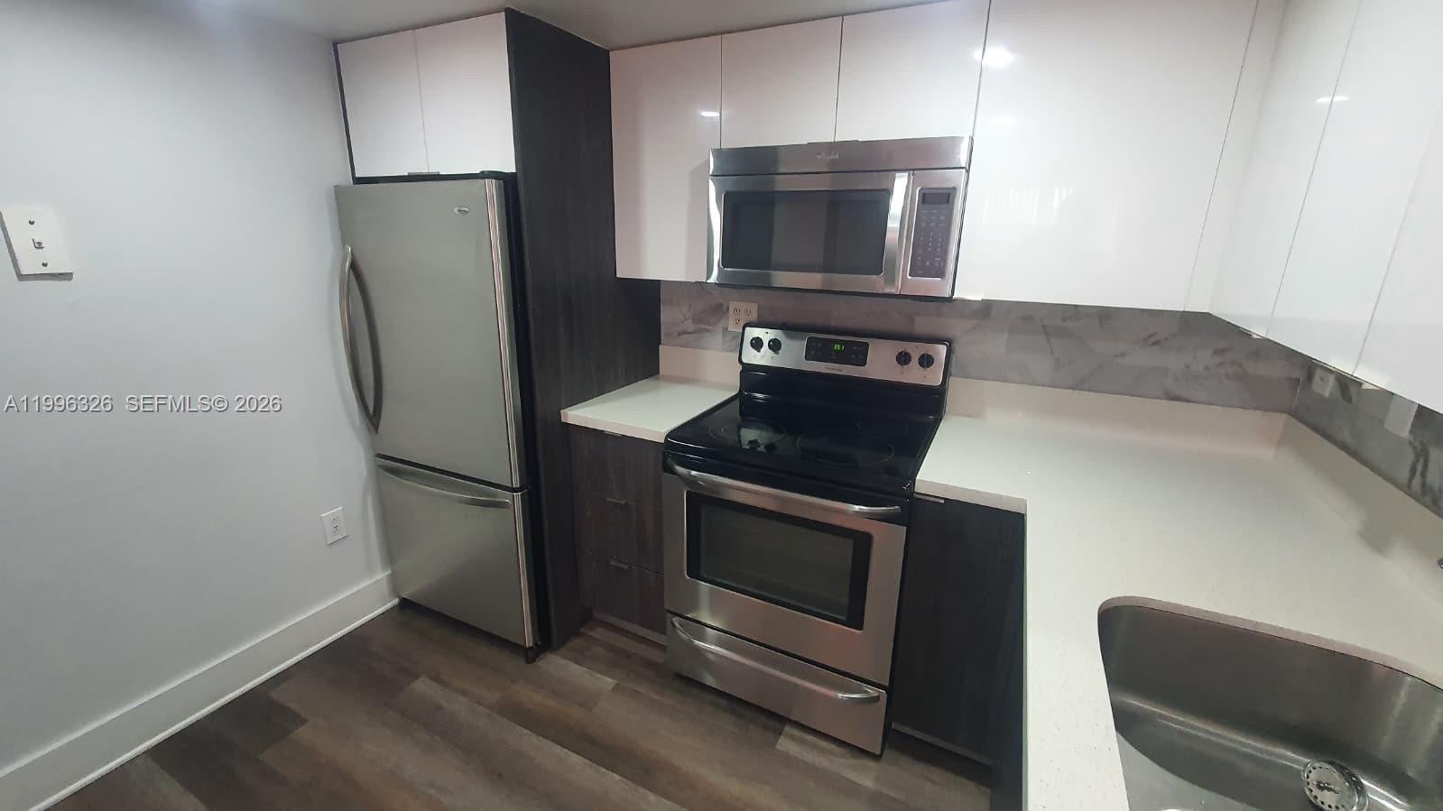 A modern kitchen features stainless steel appliances, white upper cabinets, and dark wood lower cabinets — 9885 Nob Hill Ct # 9885, Sunrise FL 33351, SUNRISE, FL