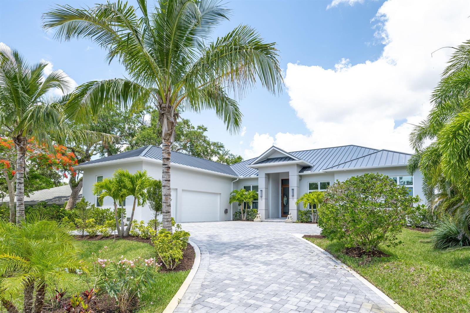 A single-story house with a metal roof, white exterior, and a paved driveway with palms — 3937 Indian River Drive E, Vero Beach FL 32963, VERO BEACH, FL