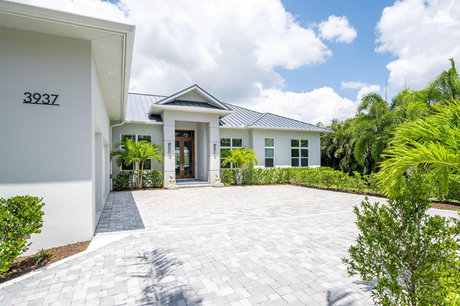 A modern house exterior features a gray metal roof, white stucco walls, and a paved driveway — 3937 Indian River Drive E, Vero Beach FL 32963, VERO BEACH, FL