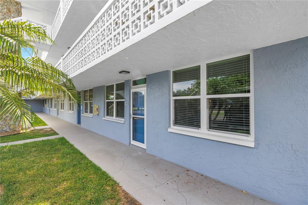 A ground-level exterior view of a blue apartment building with a concrete walkway and windows — 4715 BAY STREET NE UNIT 135, ST PETERSBURG, FL