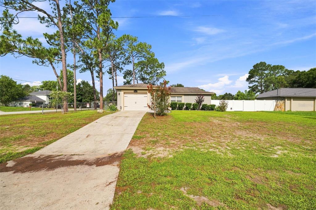 A single-story house with a concrete driveway and a large front lawn under a blue sky — 2077 ARBUCKLE ROAD, SPRING HILL, FL