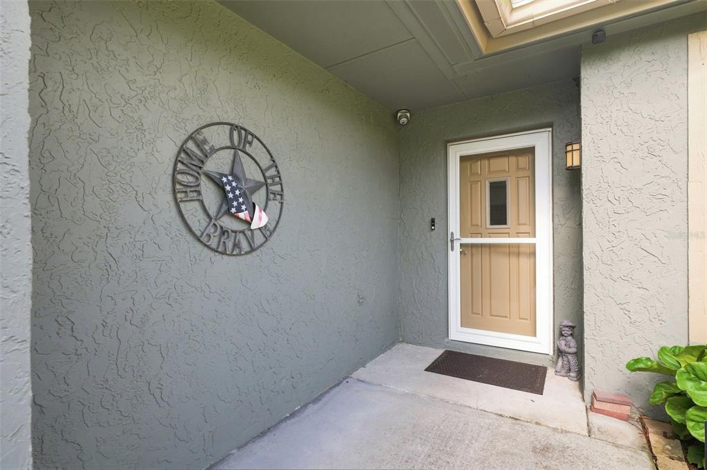A covered entryway features a tan storm door, a star wall decoration, and concrete flooring — 2077 ARBUCKLE ROAD, SPRING HILL, FL