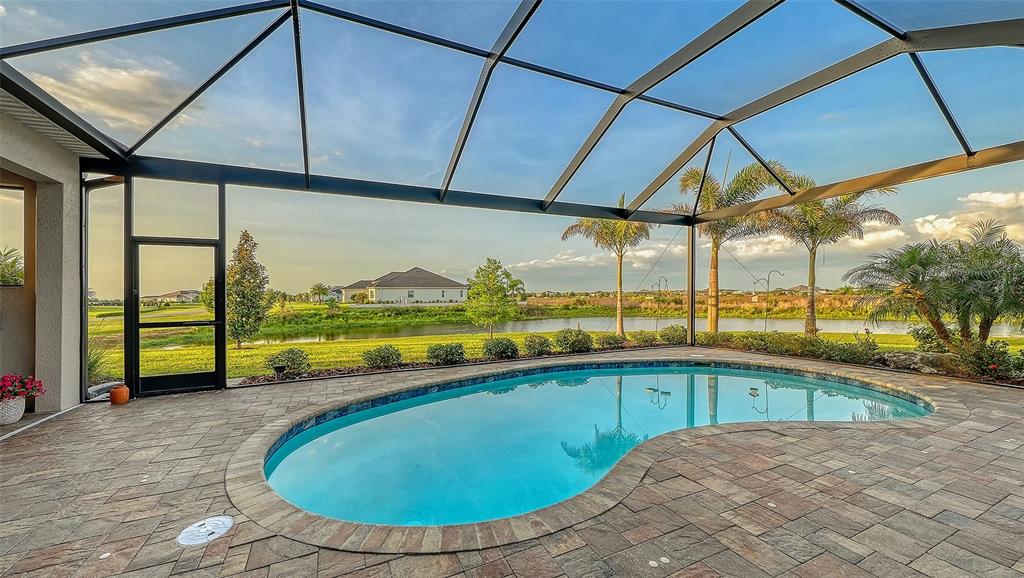 A kidney-shaped swimming pool sits on a paved patio enclosed by a screened lanai — 3554 RECURVE CIRCLE, SARASOTA, FL