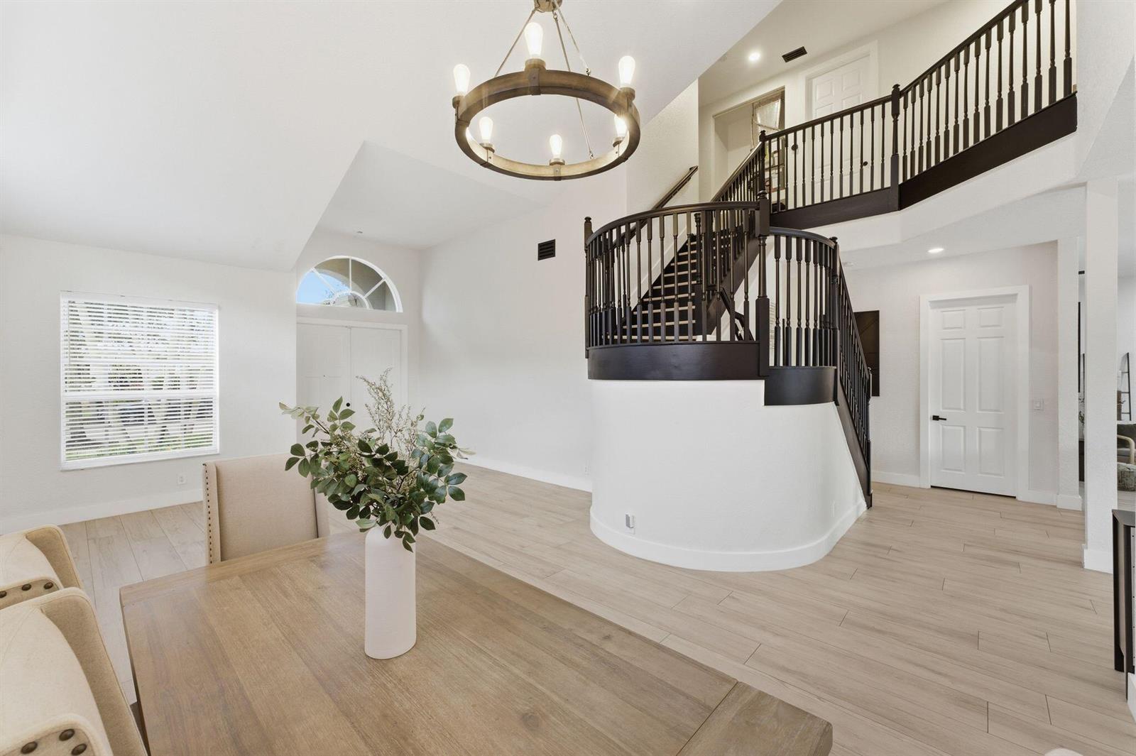 A dining area with light wood floors features a curved staircase and a wagon wheel chandelier — 12339 NW 77th Manor, Parkland FL 33076, PARKLAND, FL