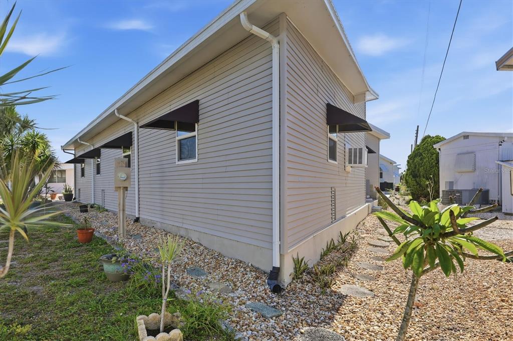 The exterior side of a light-gray vinyl-sided house features black window awnings and gravel landscaping — 2108 ILLINOIS AVENUE, BRADENTON, FL