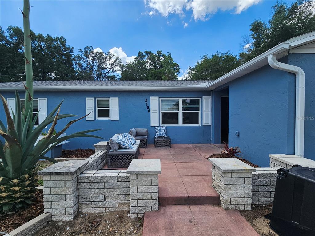 A blue house exterior features a red concrete patio, stone retaining walls, and white shutters — 8198 SE 164TH PLACE, SUMMERFIELD, FL
