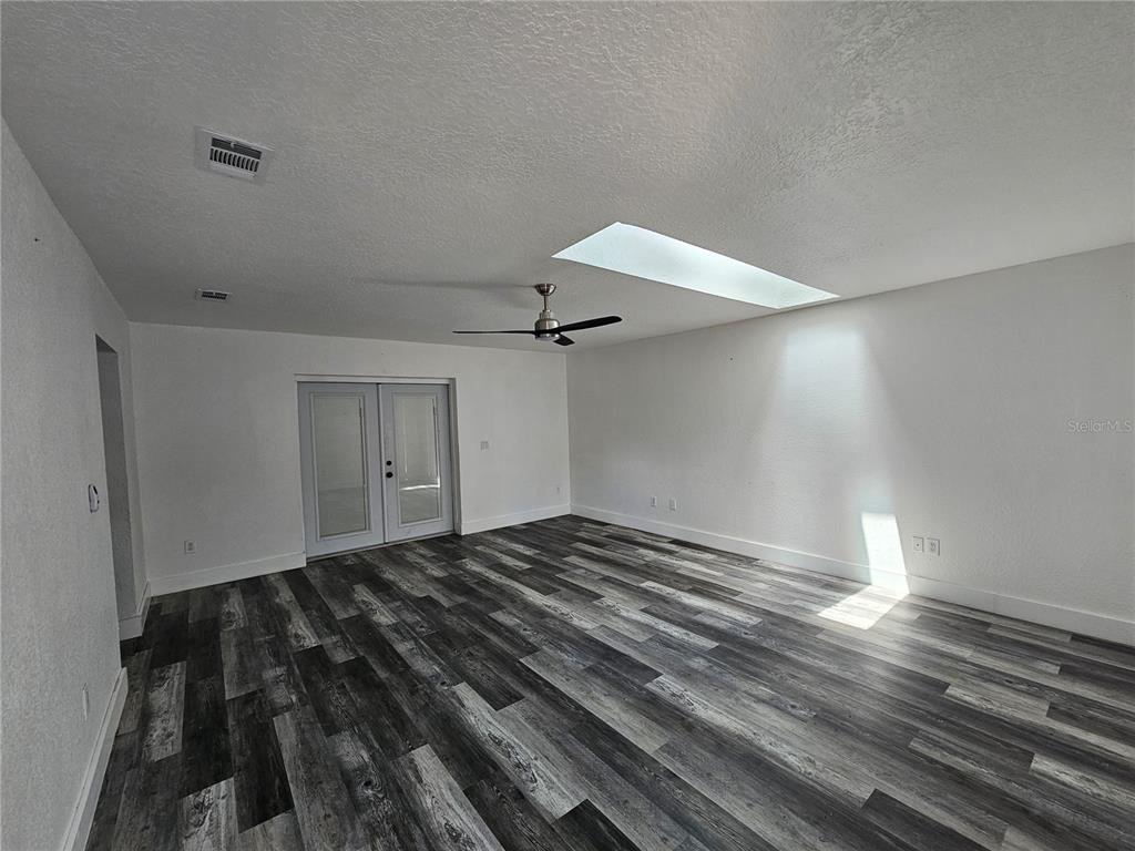 An empty room features gray wood-look flooring, a ceiling fan, and a large skylight — 8198 SE 164TH PLACE, SUMMERFIELD, FL
