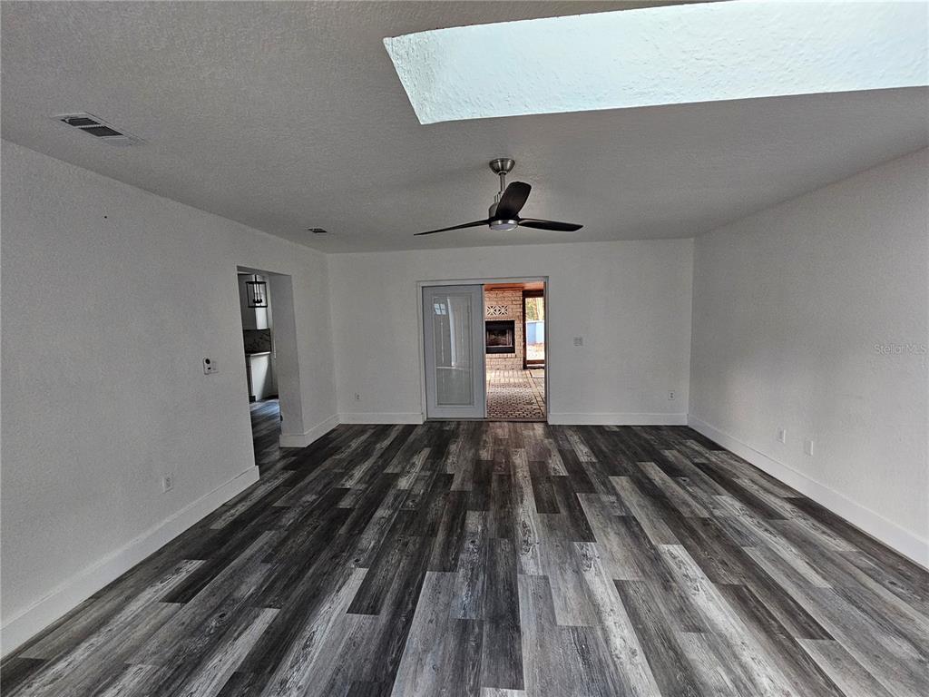 A living room features white walls, gray wood-look flooring, a ceiling fan, and a skylight — 8198 SE 164TH PLACE, SUMMERFIELD, FL