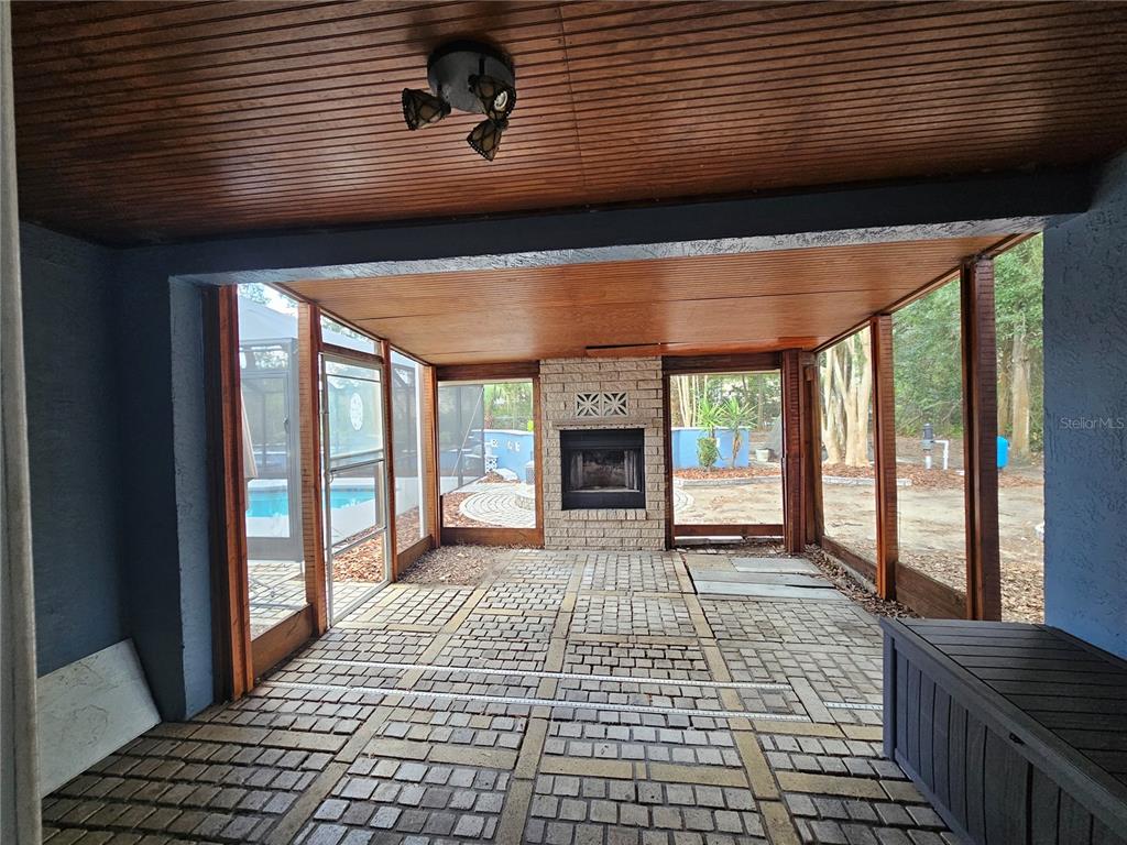 A screened-in patio features a brick fireplace, wood-paneled ceiling, and a paved brick floor — 8198 SE 164TH PLACE, SUMMERFIELD, FL