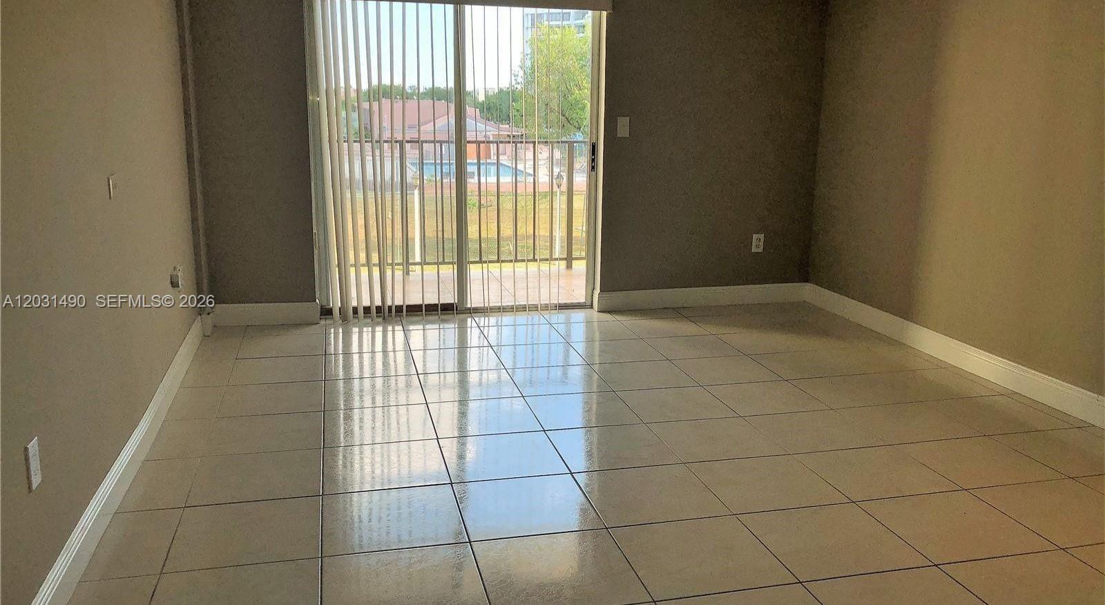 An empty room features light-colored tile flooring, beige walls, and a sliding glass door — 14250 SW 62nd St # 325, Miami FL 33183, MIAMI, FL